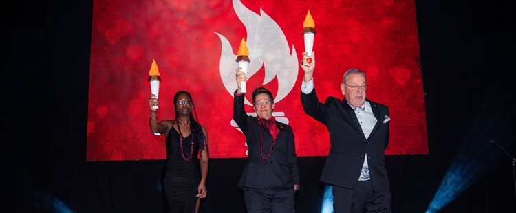 Three people on stage holding up lit torches.